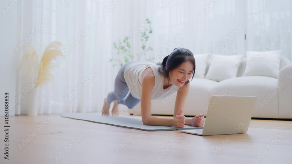 Young Asian woman in sportswear doing plank on training mat while watching online workout tutorials on laptop in the living room. Sport and recreation concept Young Asian woman in sportswear doing plank on training mat while watching online workout tutorials on laptop in the living room. Sport and recreation concept