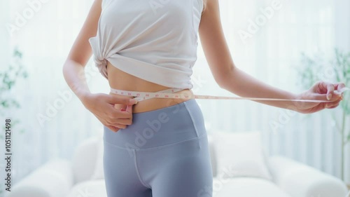 Young Asian woman in sportswear measuring her waist with a tape. Diet and healthy concept. Body shape slim