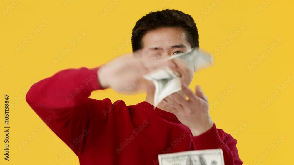 A cheerful young Asian man joyfully waves a stack of cash in his hand, surrounded by a vibrant yellow background, radiating confidence and excitement about wealth. A cheerful young Asian man joyfully waves a stack of cash in his hand, surrounded by a vibrant yellow background, radiating confidence and excitement about wealth.