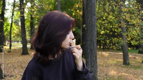 Teenage girl with striking looks playfully savors creamy ice cream cone in autumn park, tongue piercing adding hint of intrigue.