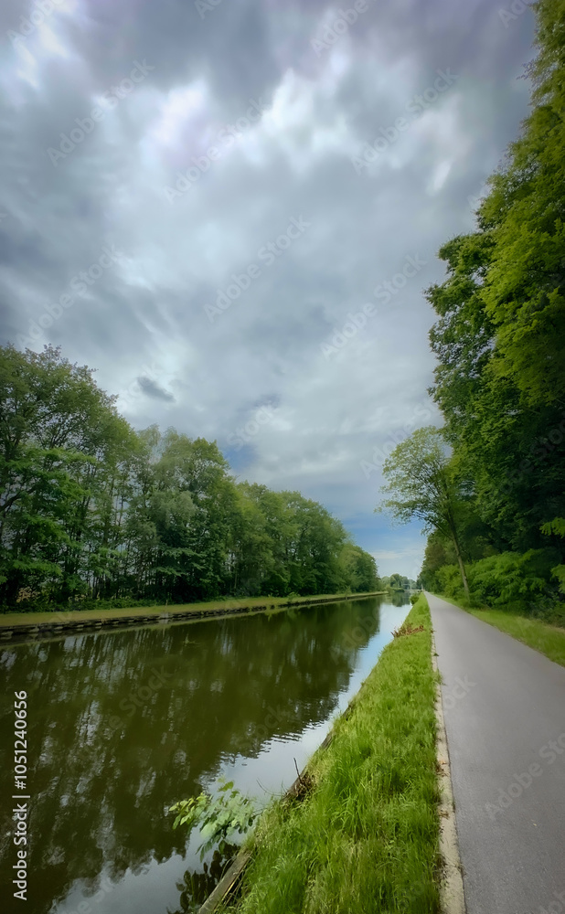 Obraz premium A serene riverbank with vibrant trees, fluffy clouds, and lush greenery is ideal for naturethemed activities