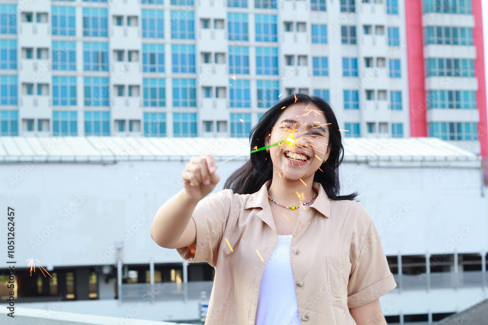 Fototapeta premium happy asian young woman holding sparklers celebrate new year eve in outdoor roof top with city building background
