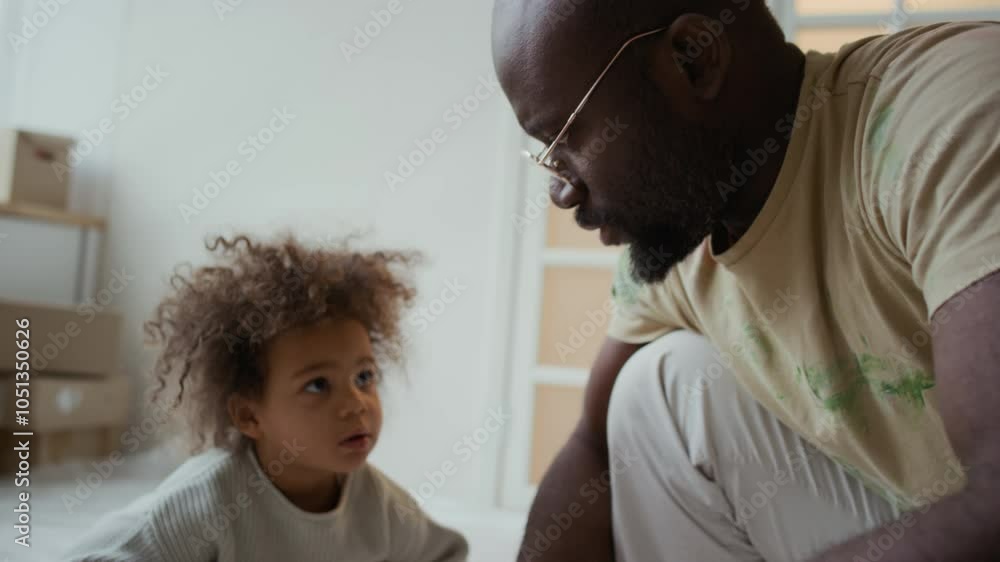 Tilt shot of African American father explaining difference of various paintbrushes to little curious Biracial daughter who sitting next to dad in room prepared for remodeling Tilt shot of African American father explaining difference of various paintbrushes to little curious Biracial daughter who sitting next to dad in room prepared for remodeling