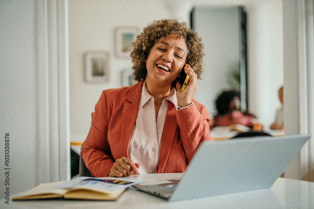 Obraz premium Successful businesswoman in modern office talking on the phone and working on a laptop