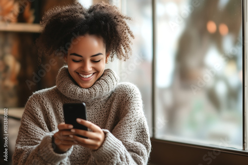 Black girl with curly hair using cell phone while smiling 