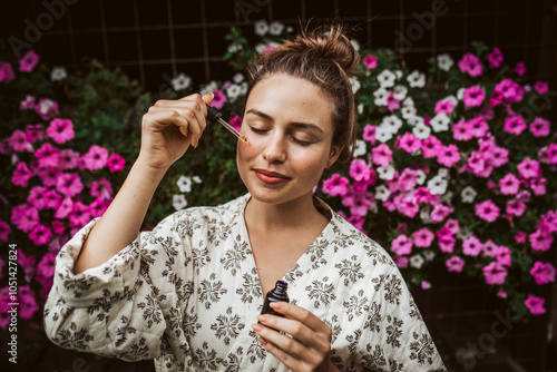 Beautiful woman doing her skin care routine outdoors, wearing bathrobe. Woman using facial skin serum with dropper. photo