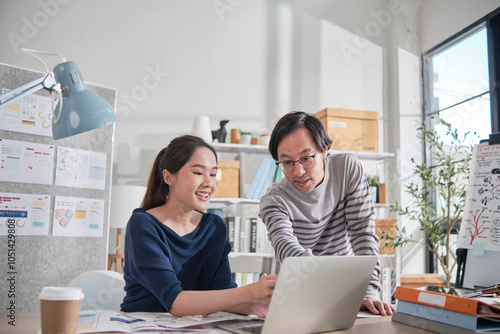 Two young Asian startup company partners discuss and brainstorm in casual small business office, marketing planning jobs on a laptop, and freelance work as E-commerce entrepreneur and coworker team.