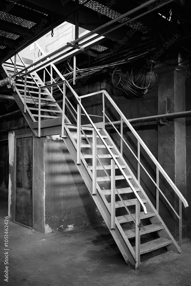 Industrial building structure fragment featuring metal staircase and pillars. Abstract image on the subject of modern architecture, industry and technology. Black and white BW shot. Industrial building structure fragment featuring metal staircase and pillars. Abstract image on the subject of modern architecture, industry and technology. Black and white BW shot.
