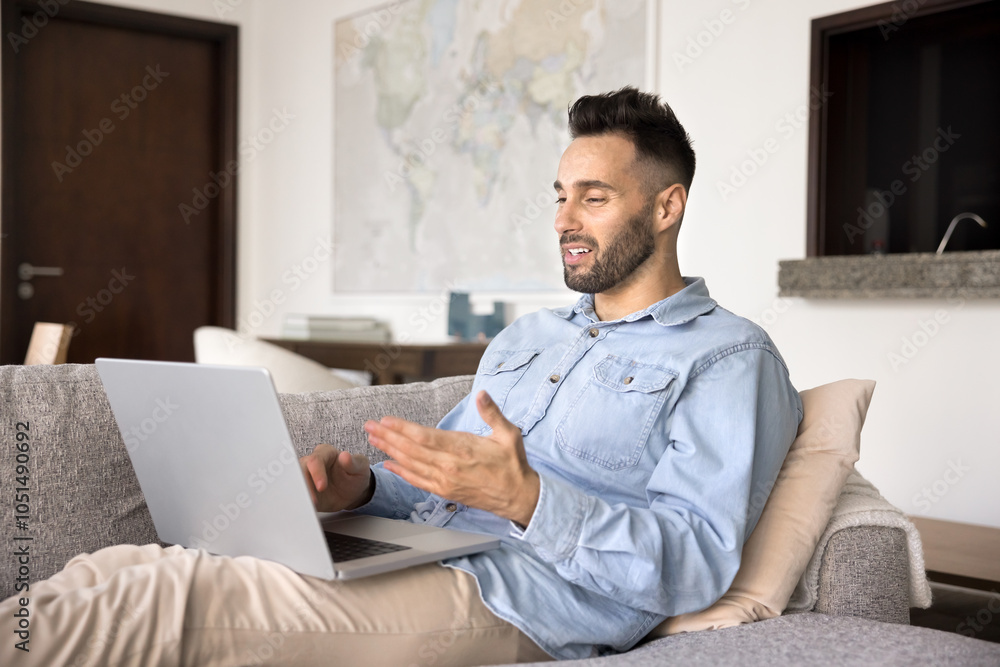 Handsome young Hispanic man talking on work conference chat at laptop, resting on home sofa, speaking on video call at computer, holding computer on lap, using pc gadget for job communication Handsome young Hispanic man talking on work conference chat at laptop, resting on home sofa, speaking on video call at computer, holding computer on lap, using pc gadget for job communication