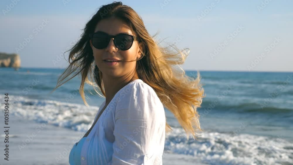 Young woman walking and spinning on sea beach on a sunny day. Beautiful girl in sunglasses touching her blonde hair and enjoying summer vacation. Concept of summer vacation or holiday. Closeup Slow mo Young woman walking and spinning on sea beach on a sunny day. Beautiful girl in sunglasses touching her blonde hair and enjoying summer vacation. Concept of summer vacation or holiday. Closeup Slow mo