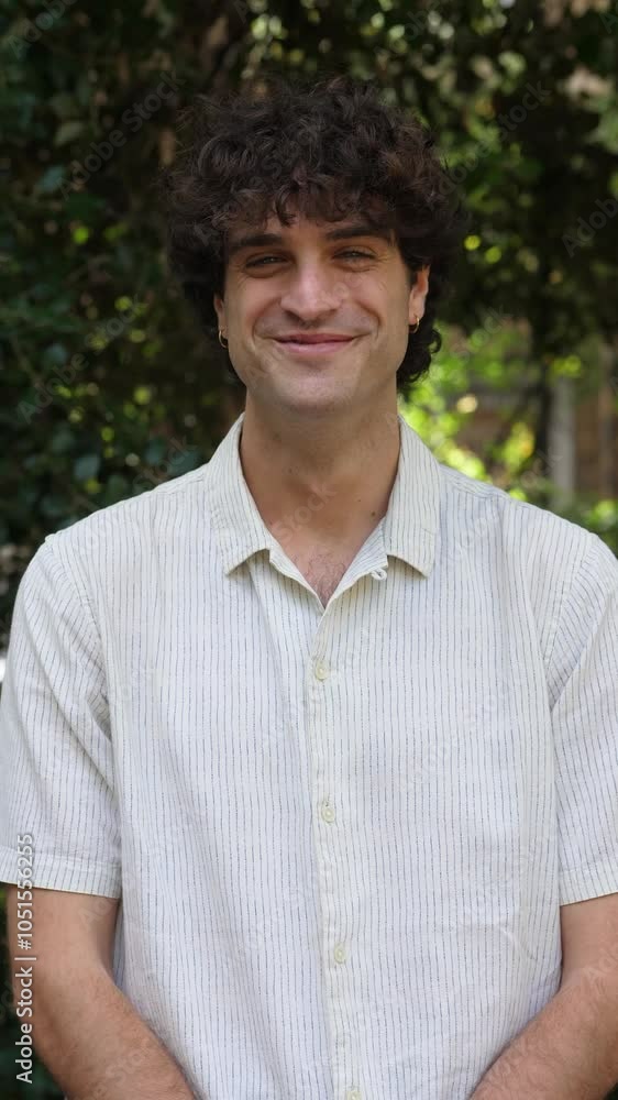 Vertical: A young man in a white shirt smiles warmly at the camera, exuding happiness and confidence in a casual setting. Vertical: A young man in a white shirt smiles warmly at the camera, exuding happiness and confidence in a casual setting.