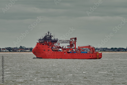 Red offshore support vessel sailing in port on a cloudy day. photo