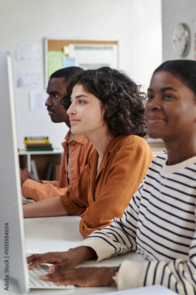 Portrait of diverse group of young professionals collaborating and using computer in modern office environment with books and clock visible in background Portrait of diverse group of young professionals collaborating and using computer in modern office environment with books and clock visible in background