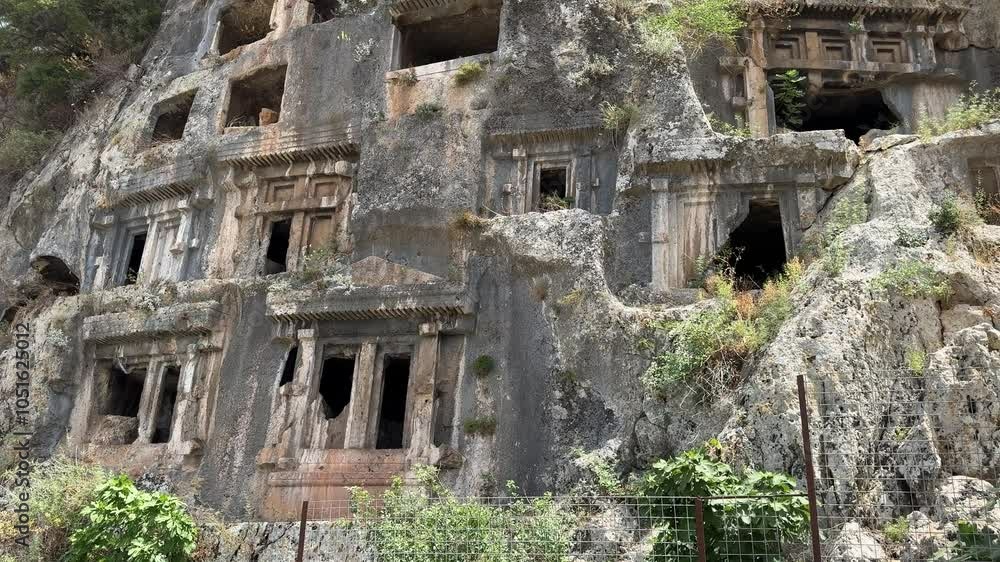 Weathered ruins of Amyntas Rock Tombs with moss growth and plants on it, on a sunny day Weathered ruins of Amyntas Rock Tombs with moss growth and plants on it, on a sunny day