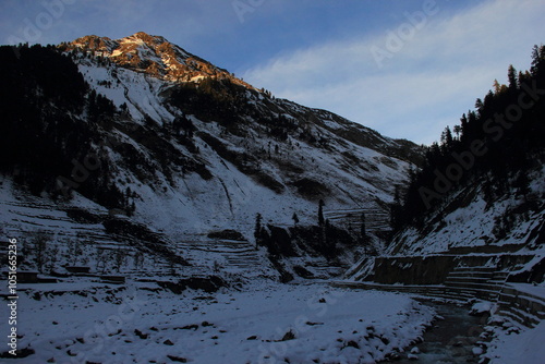 A top of a mountain, receiving first rays of the sun at the dawn, with a down hill valley after winter snowfall photo