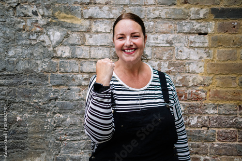 Smiling mature woman showing fist in front of brick wall photo