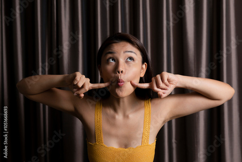 Playful woman in sleeveless yellow top puckering in front of curtain at photo booth photo