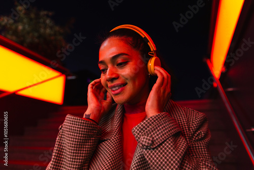 Smiling woman listening music on headphones at illuminated subway station
