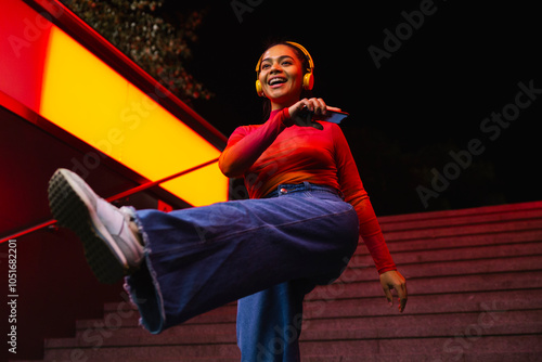 Happy woman with smart phone listening music on headphones and dancing at night