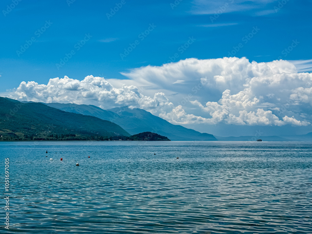 Tourist boats floating on calm Lake Ohrid in North Macedonia. Rolling hills covered in lush green vegetation. Tranquil lakeside scene. Summer travel destination in the Balkans. Boat tour tourism Tourist boats floating on calm Lake Ohrid in North Macedonia. Rolling hills covered in lush green vegetation. Tranquil lakeside scene. Summer travel destination in the Balkans. Boat tour tourism