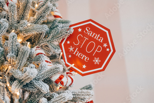 A festive sign asking Santa to stop at the decorated Christmas tree photo