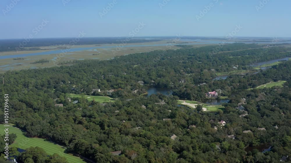 A static aerial shot of Kiawah Island, South Carolina, showcasing lush green forests, golf courses, and serene waterways in a peaceful landscape. A static aerial shot of Kiawah Island, South Carolina, showcasing lush green forests, golf courses, and serene waterways in a peaceful landscape.