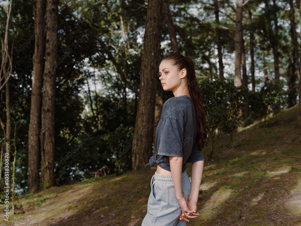 Fototapeta premium Thoughtful young woman standing in a serene forest setting, wearing a relaxed outfit, looking contemplative and embracing nature s tranquility