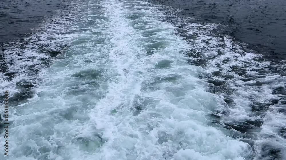 Boat wake trailing across deep blue ocean waters on a cloudy day, creating foamy white patterns Boat wake trailing across deep blue ocean waters on a cloudy day, creating foamy white patterns