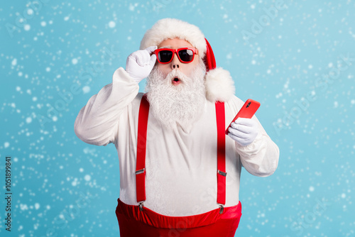 Photo of pensioner grandfather grey beard hold telephone read fake news christmas cancelled wear santa x-mas red costume suspenders sunglass white gloves cap isolated blue color background