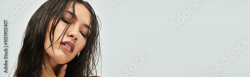 A stunning young woman with wet hair showcases her beauty and confidence in a tranquil studio.