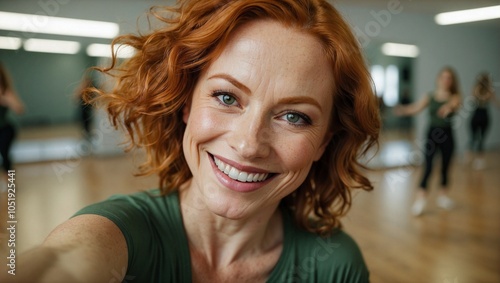 Smiling Caucasian woman with red hair takes a selfie in a dance studio, exuding energy and positivity.