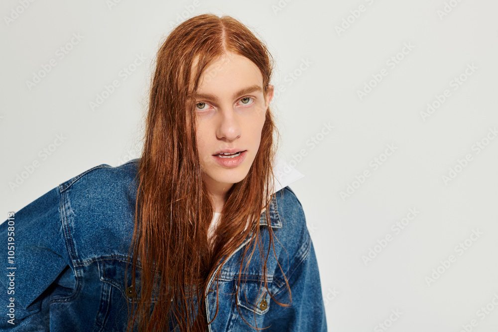 A teenage boy with striking long red hair poses stylishly in a denim outfit against a neutral backdrop. A teenage boy with striking long red hair poses stylishly in a denim outfit against a neutral backdrop.