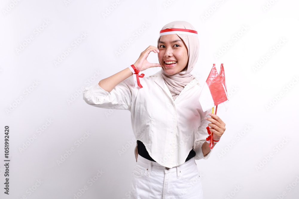 Happy smiling Indonesian muslim woman holding Indonesia's flag and showing love sign to celebrate Indonesia Independence Day isolated over white background. Happy smiling Indonesian muslim woman holding Indonesia's flag and showing love sign to celebrate Indonesia Independence Day isolated over white background.