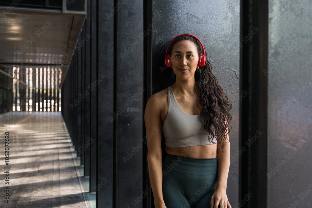 Naklejka premium Latin sportswoman wearing headphones relaxing after workout session