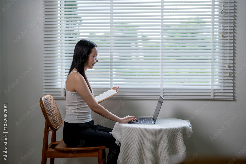 Young asian woman working from home using laptop and taking notes Young asian woman working from home using laptop and taking notes