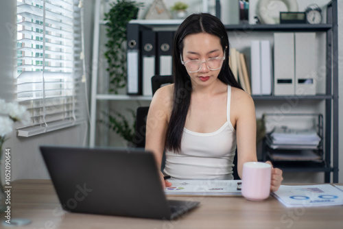 Young asian woman working at home office holding coffee mug Free Download Young asian woman working at home office holding coffee mug - GFXLoad