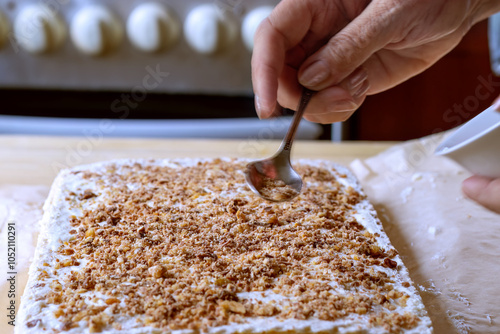 Woman's hand sprinkling top of cake. Decorating top of cake with crumbs of mixture of chocolate, nuts and caramel. Close-up. Decorating top of Napoleon cake.