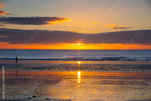 A landscape of a golden sunset with the sun partially covered by clouds reflecting in the sea off Dinas Dinlle beach, North Wales photo