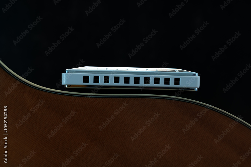 Macro close up diatonic harmonica lying on side of guitar body showing the curve of the guitar body