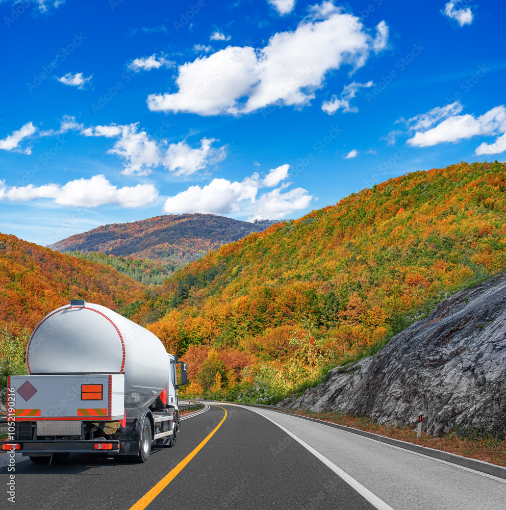 Fuel truck on a picturesque road against the backdrop of an autumn landscape. A tank truck transports fuel.