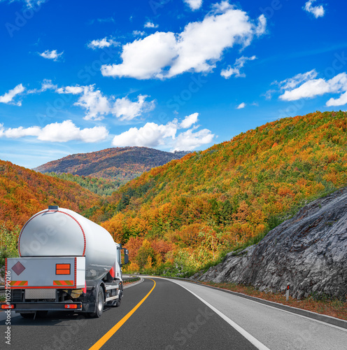 Obraz na płótnie Fuel truck on a picturesque road against the backdrop of an autumn landscape. A tank truck transports fuel. w salonie