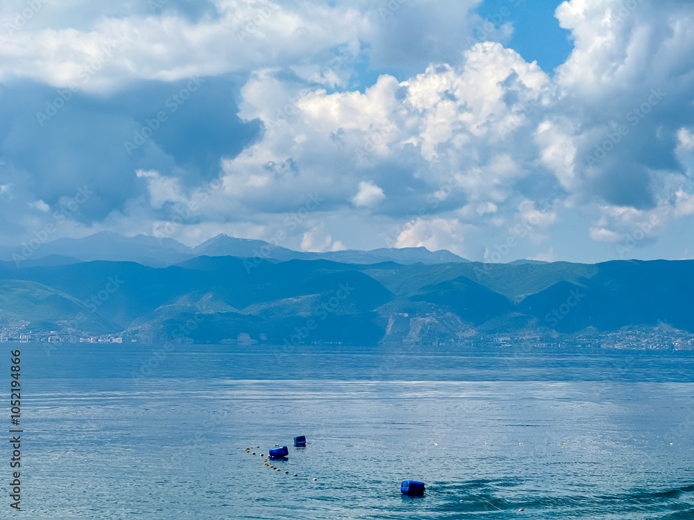 Obraz premium Serene lakeside scene along the shoreline of Lake Ohrid, North Macedonia. Mountain range of National Park Galicica in the distance. Slopes and hills covered with lush green vegetation and forest