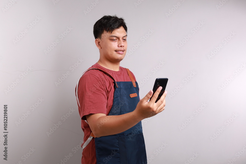 Young man barista bartender barman employee in blue apron white t-shirt work in coffee shop using mobile cell phone chat isolated on white background studio portrait. Small business startup concept Young man barista bartender barman employee in blue apron white t-shirt work in coffee shop using mobile cell phone chat isolated on white background studio portrait. Small business startup concept