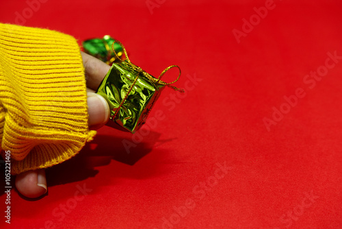 Christmas gift box and shadow shown with fingers on red paper background. Xmas holiday background with concept of winter, small gift, green box, celebration, unwrap, sweater, present, red and green. photo