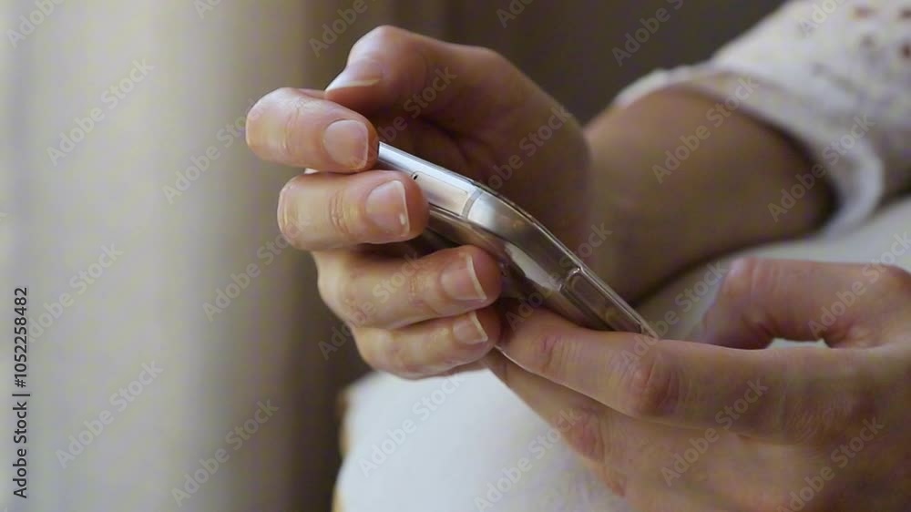 Close up of a young woman holding her smartphone in the comfort of her home, scrolling through social media, reading, writing or shopping online.