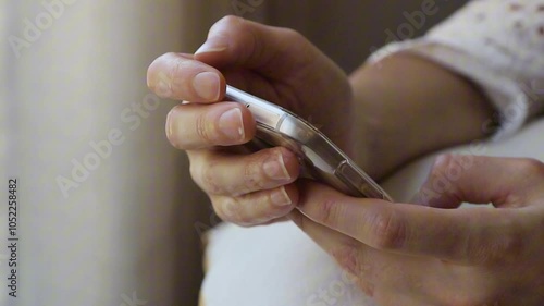 Close up of a young woman holding her smartphone in the comfort of her home, scrolling through social media, reading, writing or shopping online.