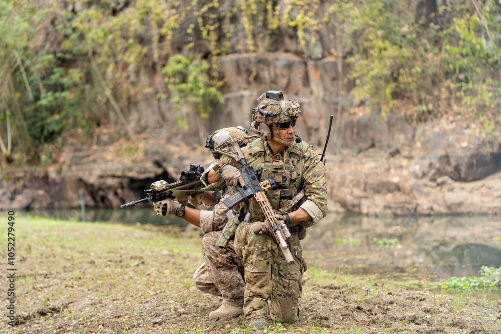 Two of militaries or soldiers stay in battlefield near the river with holding gun also look to different direction during outdoor practice. Two of militaries or soldiers stay in battlefield near the river with holding gun also look to different direction during outdoor practice.