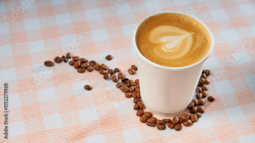Takeaway coffee paper cup with coffee beans on a checkered background. Milk foam heart