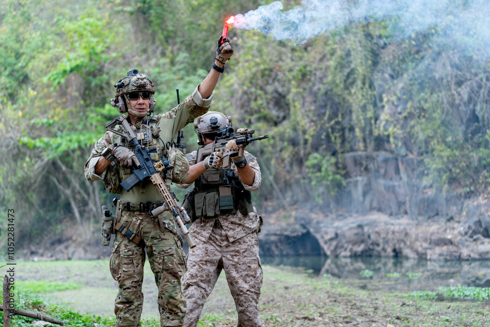 Two militaries or soldiers stay in battlefield near the river with one hold flare fireworks and one stand with point gun forward direction during outdoor practice. Two militaries or soldiers stay in battlefield near the river with one hold flare fireworks and one stand with point gun forward direction during outdoor practice.