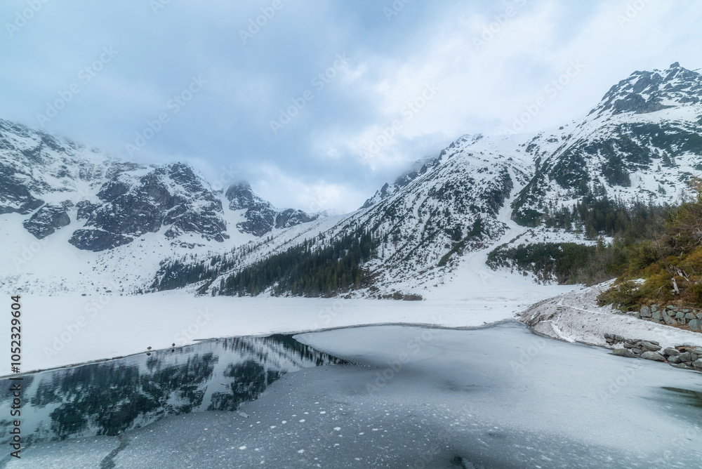 Obraz premium tranquil view of Morskie Oko in Tatra National Park, Poland, showcasing majestic snow-covered mountains, serene frozen lake, and reflections on a chilly winter day. Winter landscape